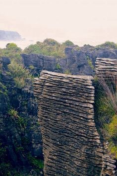 some very tall rocks by the water and grass in the foreground, with an island in the background