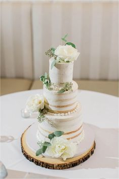 a three tiered wedding cake on top of a wooden slice with white flowers and greenery