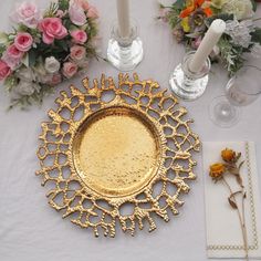 a gold plate sitting on top of a table next to some flowers and napkins