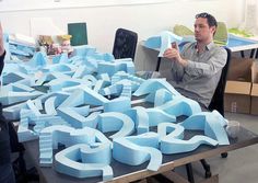 two men are working on letters made out of blue foams at a table in an art studio