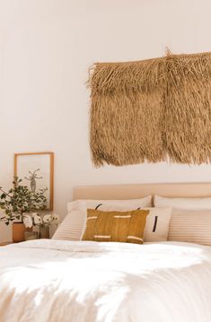 a bed with white sheets and pillows in a bedroom next to a wall hanging over the headboard