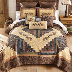 a bed covered in a brown and tan quilt next to a night stand with a lamp on it