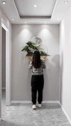 a woman standing in front of a mirror holding a plant on top of a shelf