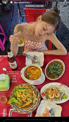 a woman sitting at a red table with food and drinks in front of her on the phone