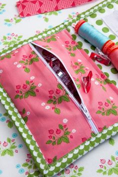 sewing supplies sitting on top of a pink flowered cloth covered in green and white flowers