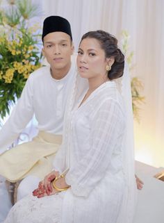 a man and woman sitting next to each other in front of a vase with flowers