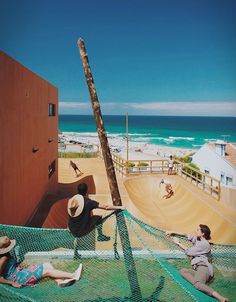 two people sitting on the ground near a fence with a beach and ocean in the background