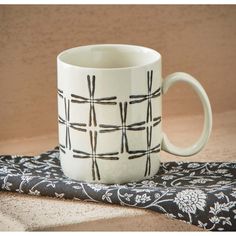 a white coffee mug sitting on top of a black and white table cloth next to a brown wall