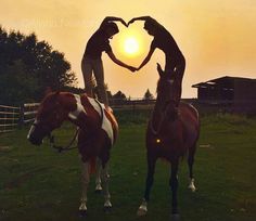 two people standing on horses making a heart shape with their hands in front of the sun