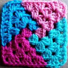 a crocheted square is shown with pink, blue and green squares on it