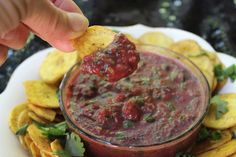 a person dipping salsa into a bowl with tortilla chips