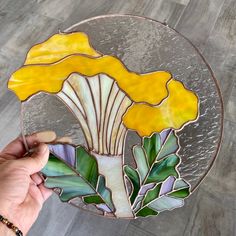 a hand holding up a stained glass plate with a yellow flower on it and leaves