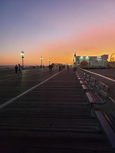 people are walking on the boardwalk at sunset or dawn with benches in front of them