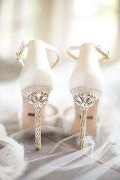 two pairs of white high heeled shoes sitting on top of a pile of yarn