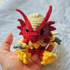 a crocheted red and yellow dragon doll is held in someone's hand