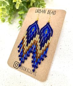 Dazzle with our Boho-chic, handcrafted Blue and Gold Fringe Seed Bead Earrings. Precisely strung to create a striking gold and black contrast, these earrings are an accessory that speaks volumes. Lightweight, they add elegance to any outfit without weighing you down. Crafted for durability with high-quality seed beads and strong thread, we prioritize both style and comfort. A perfect gift for any occasion or a delightful treat for yourself, these earrings add a touch of sophistication to any out Bohemian Blue Long Drop Beaded Earrings, Artisan Blue Beaded Earrings As Gift, Blue Long Drop Beaded Earrings As Gift, Blue Long Drop Beaded Earrings For Gift, Handmade Artisan Blue Beaded Earrings, Artisan Blue Earrings With Dangling Beads, Adjustable Blue Beaded Chandelier Earrings, Artisan Blue Beaded Earrings With Colorful Beads, Handmade Blue Teardrop Chandelier Earrings