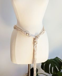 a white mannequin with a silver chain belt on it's waist, next to a potted plant