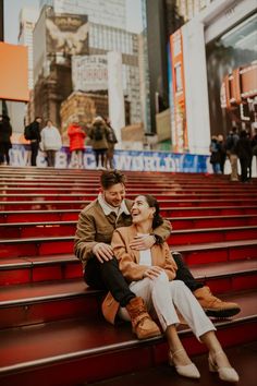 a man and woman are sitting on the steps in front of some red stairs with people walking by