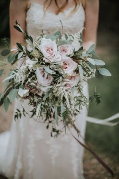 a bridal holding a bouquet of pink roses and greenery in her hands,