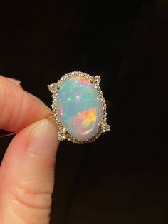 Stunning oval opal cabochon weighing 10.6 carats of mesmerizing hot pinks, red, orange and neon hues. The opal is 10 mm in depth/height is held by 4 tall prongs with bezel accented with 36 dainty diamonds. A larger round faceted cut diamond is placed at the base of each prong. Slim simple 14k solid yellow gold band for comfortable wear. Gorgeous timeless piece of jewelry!  Stone: Ethiopian opal, diamonds Stone weight: 10.6 carats Stone size: 18 x 12 mm  Stone shape: sphere Metal: 14K yellow gold Metal weight: 4.32 grams We gladly accept custom orders using either our designs or design of your choice with stones from our collection or your own.  Please contact us directly for details.  Please feel free to visit my shop for additional pieces of high end natural gemstone jewelry: https://www. Elegant Ethiopian Opal Ring With Oval Cabochon, Yellow Gold Ethiopian Opal Ring In Oval Cabochon Shape, Gold Ethiopian Opal Cabochon Ring, Unique Ethiopian Opal Cabochon Rings, Large Engagement Rings, Elegant Ethiopian Opal Ring, Oval Cabochon, Opal Band, Ethiopian Opal Ring, Rainbow Opal