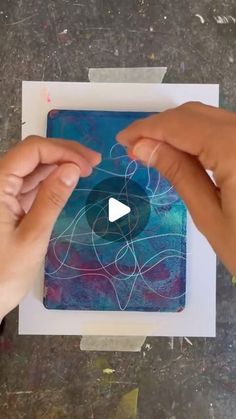 two hands holding up a piece of paper with an abstract design on it and the video below