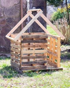 a small wooden house made out of pallet wood in the grass next to a stone wall