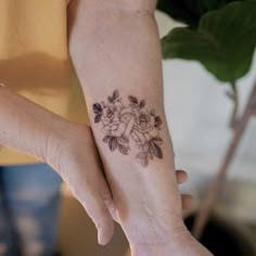 two hands holding each other with tattoos on their fingers and wrist, one has a flower tattoo on it