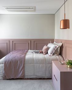 a bed with pink sheets and pillows in a bedroom next to a lamp on the wall