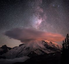 the night sky is filled with stars and clouds above a snow covered mountain, as seen from below