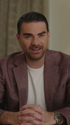 a man sitting at a table with his hands folded out and looking into the camera