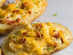 two baked potatoes with cheese and bacon on them sitting on a white counter top next to some slices of bread