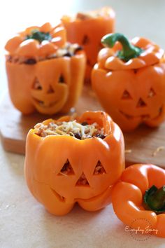 four carved pumpkins sitting on top of a cutting board next to some green peppers