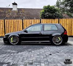 a small black car parked in front of a wooden fence with yellow rims on it