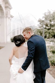 a bride and groom standing under an umbrella on the sidewalk in front of a building