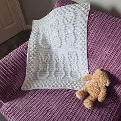 a brown teddy bear laying on top of a purple couch next to a white crocheted blanket