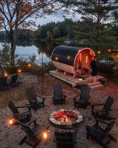 an outdoor fire pit with chairs around it and lights on the ground next to water