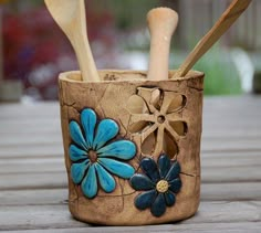 two wooden spoons in a ceramic cup with flowers and leaves on the outside side