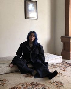 a woman with blue hair sitting on the floor next to a mattress in a room