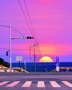 the sun is setting over the ocean with power lines and traffic lights in foreground