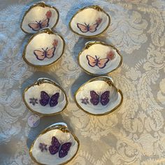 six small dishes with butterflies on them sitting on a lace covered tablecloth and gold trimming