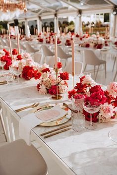 the tables are set with white linens, red and pink flowers, gold place settings and candles