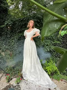 a woman standing in front of a bush wearing a white dress