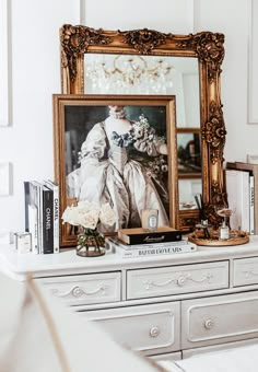 a white dresser topped with books and a framed photo next to a vase filled with flowers