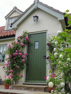 a green door with pink and white flowers on the side of a house next to some bushes