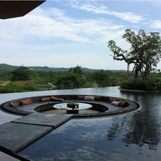 an outdoor swimming pool surrounded by trees and water features circular seating area with built - in fire pit