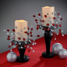 two black vases with red and silver decorations on top of a red table cloth