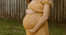 a pregnant woman in a yellow dress poses for the camera with her hand on her belly