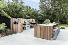 an outdoor kitchen with wooden cabinets and grilling area in the back yard, surrounded by trees