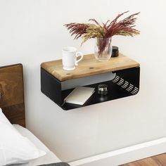 a wooden shelf with a book, coffee cup and plant on it next to a bed