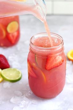 strawberry lemonade is being poured into a mason jar with limes and strawberries